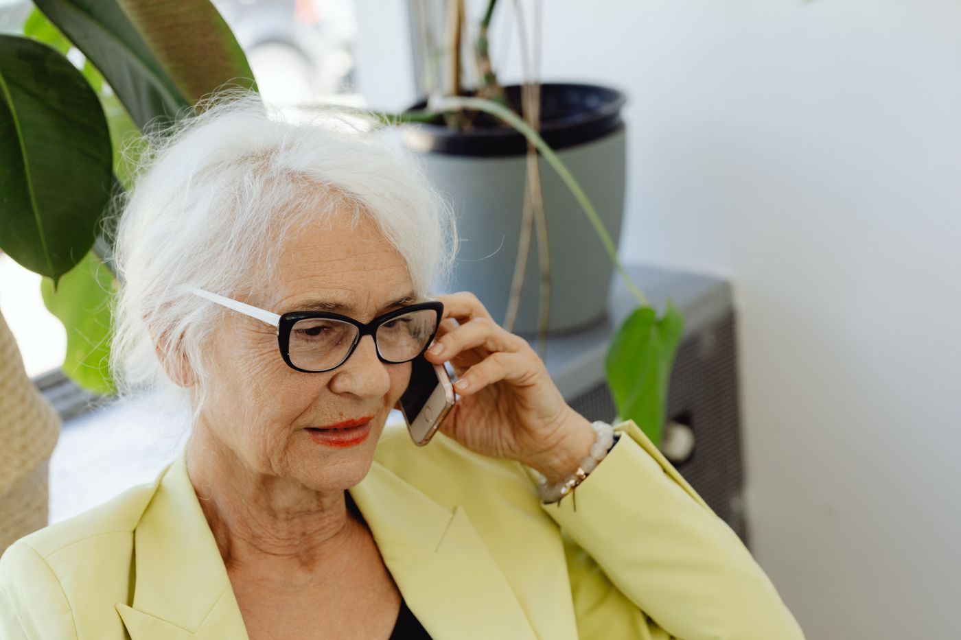 Een oudere vrouw met wit haar belt ontspannen vanuit haar eigen huis